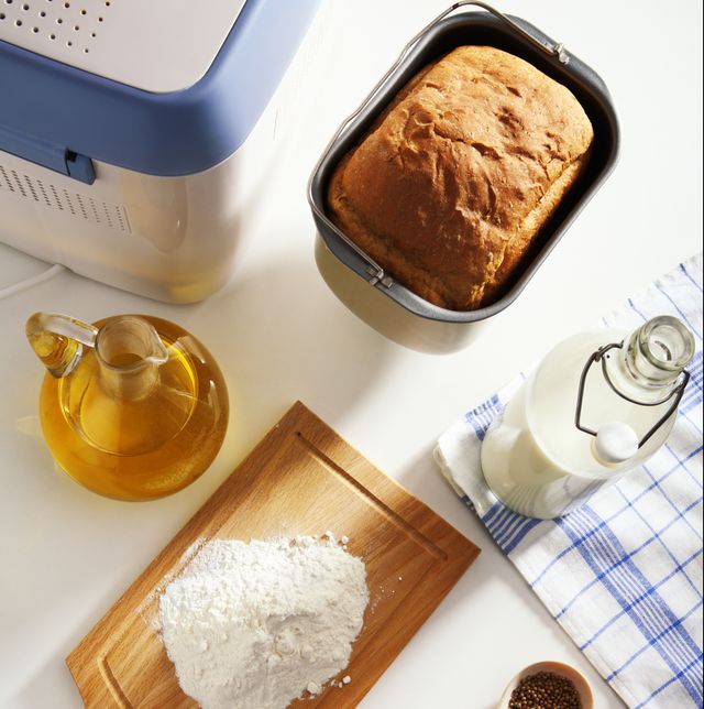 flour on a cutting board, oil and milk in bottles, bread in a breadmaking pan, and a bread machine