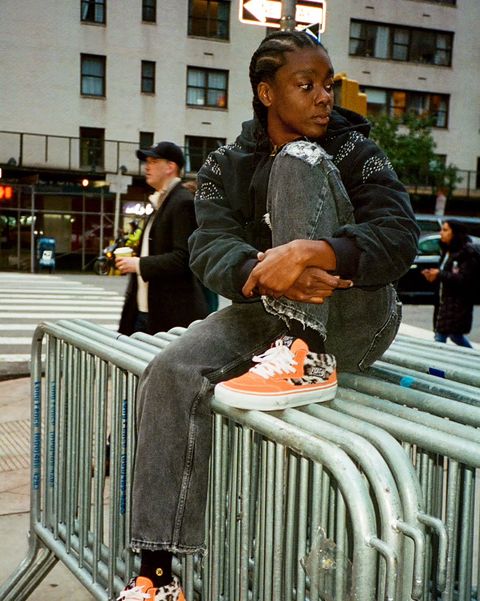 a man sitting on a railing wearing new supreme x vans sneakers