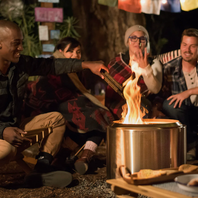 Solo Stove Bonfire a stainless steel fire pit in a backyard with people roasting food
