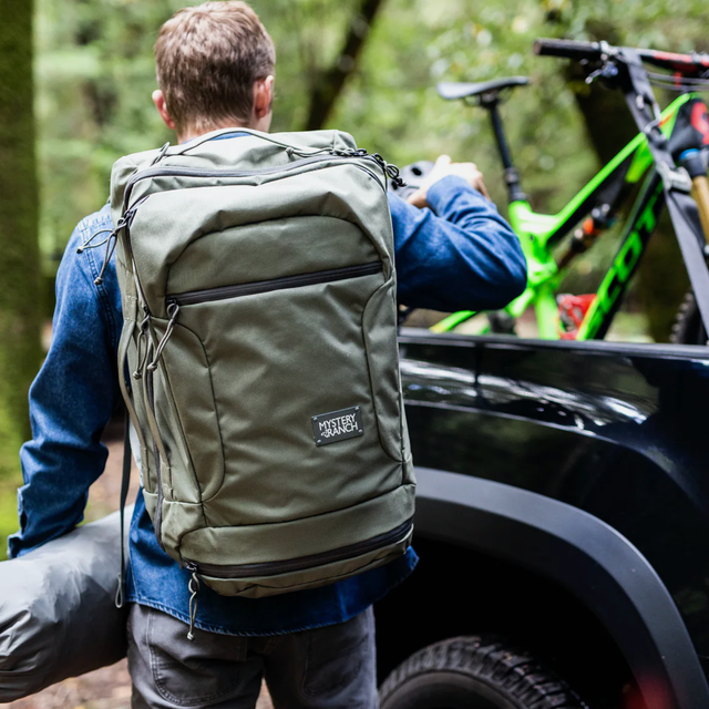 Mystery Ranch Mission Rover 43L a model loading up a truck with a backpack, bike and tent bag