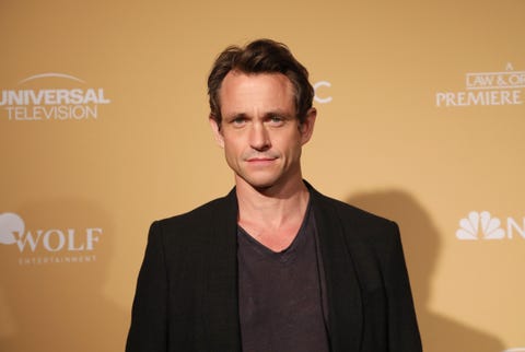 hugh dancy, a man stands looking at the camera, brown hair in loose waves around head, black tshirt and jacket