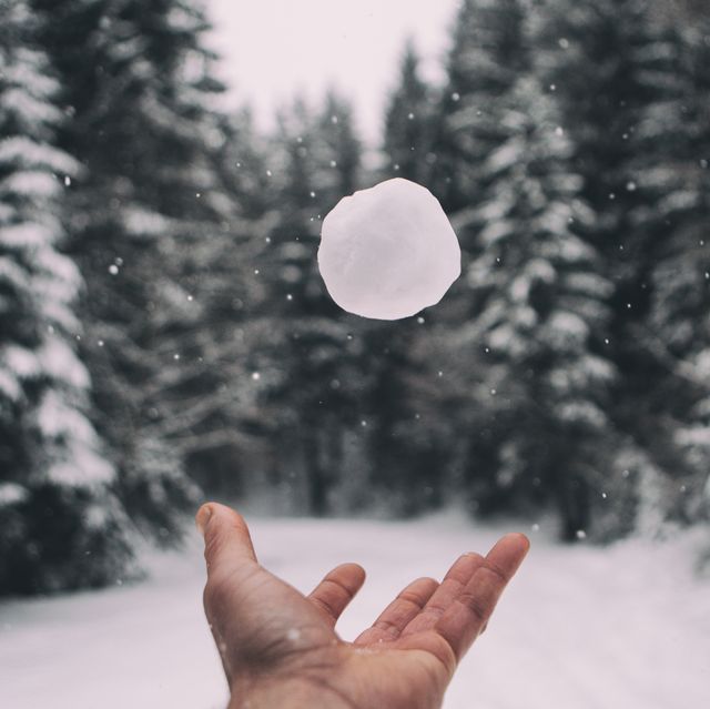 human hand throwing snowball against trees