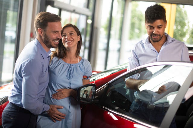 husband buying a new car together with his pregnant wife at a car dealership salon