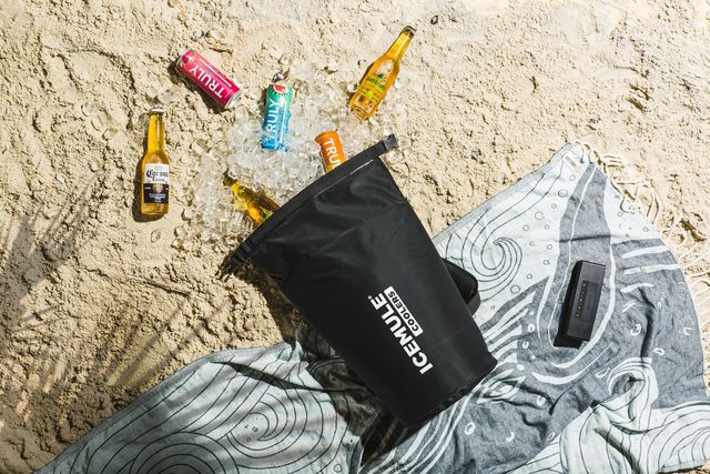 icemule cooler laying on beach towel with drinks and ice spilled ou tover sand