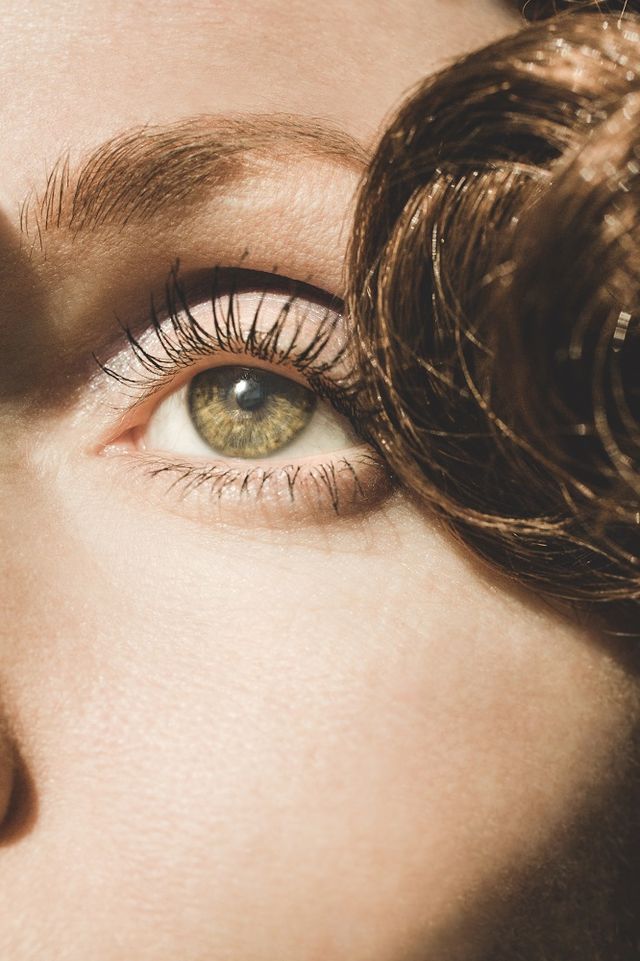 retro woman's eye closeup with long eyelashes and mascara woman has green eyes, smooth skin, thin eyebrows, and curly hair in this dreamy portrait, she is looking away from the camera