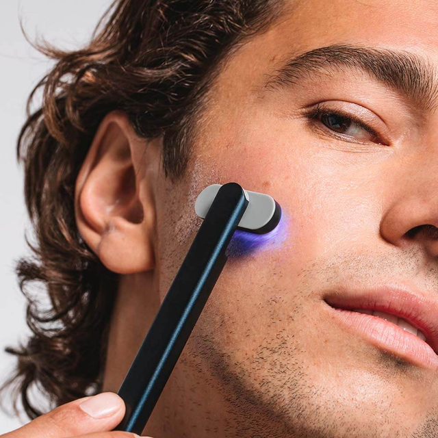 man using solawave blue light therapy wand on his cheek