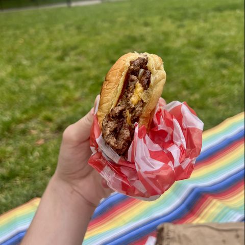hand holding double cheeseburger with red checkered paper
