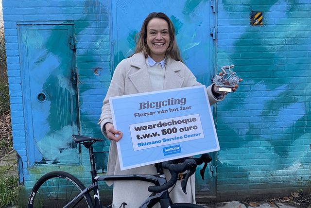 jessica de jong is de fietser van het jaar 2022 en staat met de gewonnen cheque en haar fiets voor een muurthje