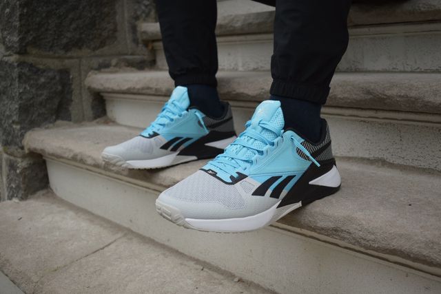 someone wearing blue, gray, and black reebok nano 6000 sneakers standing on steps