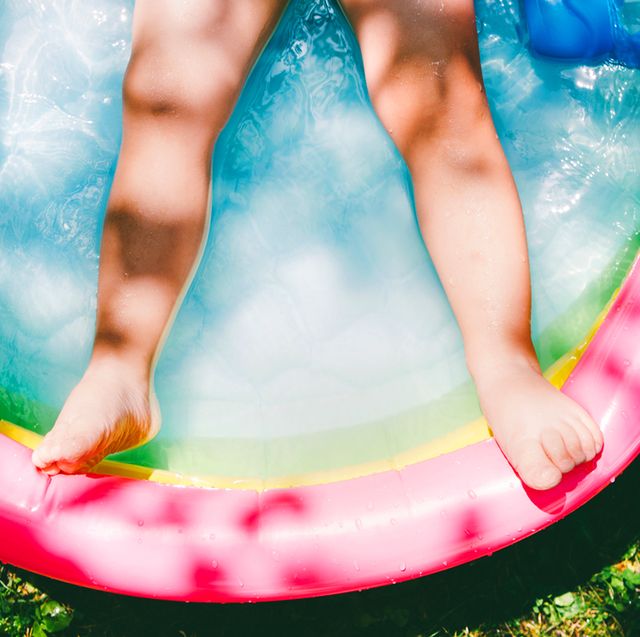 childs legs in colorful inflatable pool on grass surrounded by pool toys