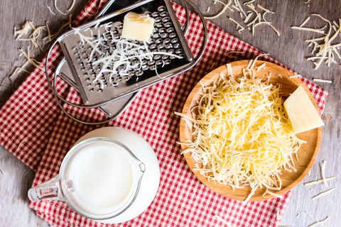 Ingredients for pasta cheese sauce or pizza, freshly grated parmesan or cheddar hard cheese, raw milk in a pot, kitchen tools, grater, wooden plate and kitchen towel, rustic vintage style, top view