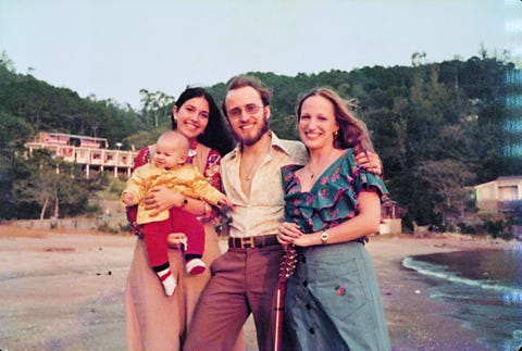 a man stands on a beach with two women and a baby