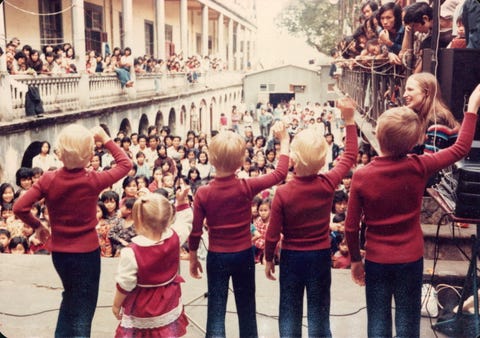 five young children in red outfits perform for a large crowd
