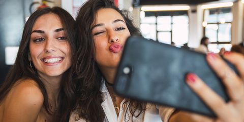 Portrait of two friends taking selfie with smartphone in a coffee shop having fun