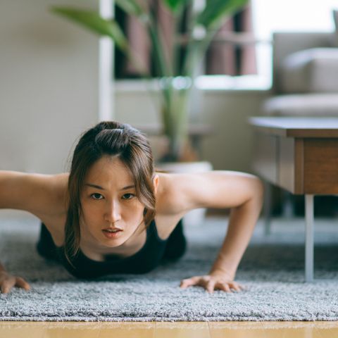 Japanese woman in fitness attire performing push-ups on floor of living room
