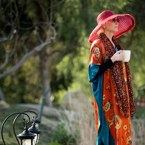 jean smart in a red sunhat and flowing orange sweater