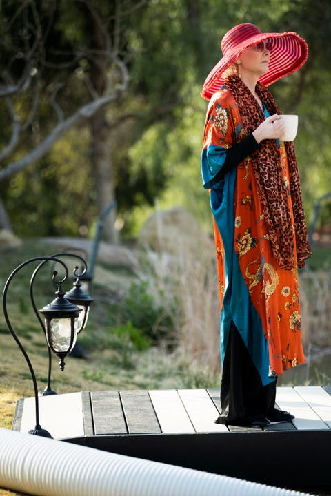 jean smart in a red sunhat and flowing orange sweater