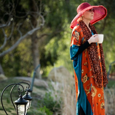 jean smart in a red sunhat and flowing orange sweater