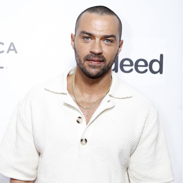 jesse williams, a man stands with hands in pockets, wearing white tshirt and grey trousers
