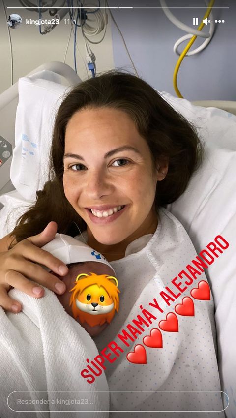 la modelo sonríe desde la cama del hospital con su bebé sobre ella