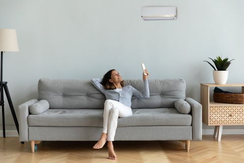 joyful mixed race woman turning on cooler system air conditioner