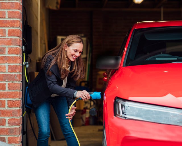 a mid adult female plugs her car in to charge and is conscious of her energy consumption and her carbon footprint