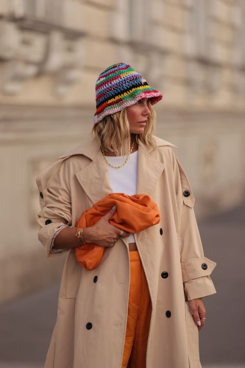 vrouw met oranje broek trenchcoat en gehaakte hoed
