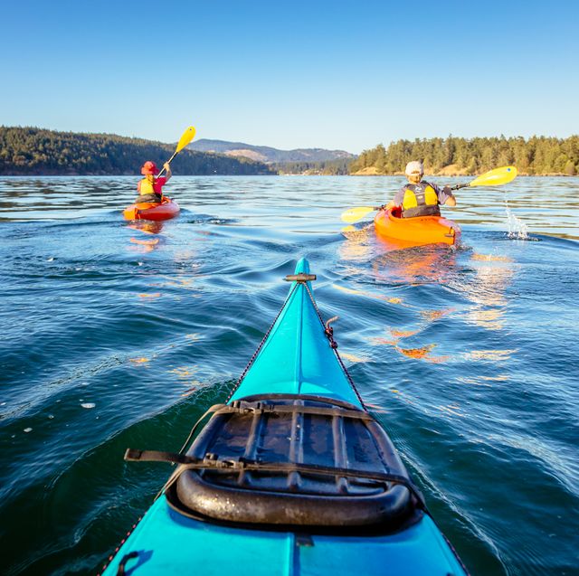 3 people kayaking on lake with mountains in background