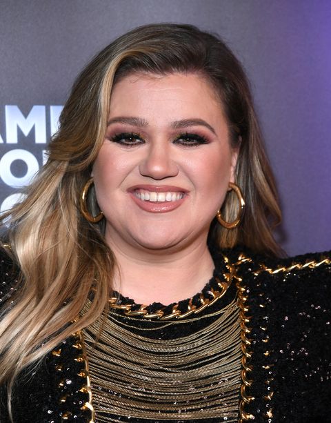 close up of kelly clarkson with long, highlighted blonde hair, dark brown eye makeup and gold hoop earrings, smiling