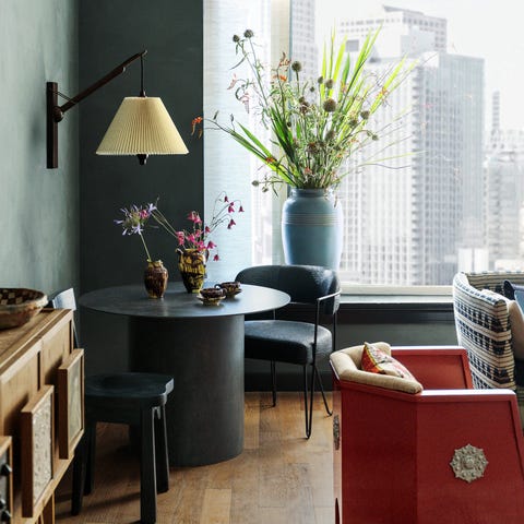 A List 2022 - ELLE DECOR proper los angeles, properhotelcom hotel room with wooden plank floors a red moroccan low seat and a black round pedestal table and chairs with large urn with flowers by the window