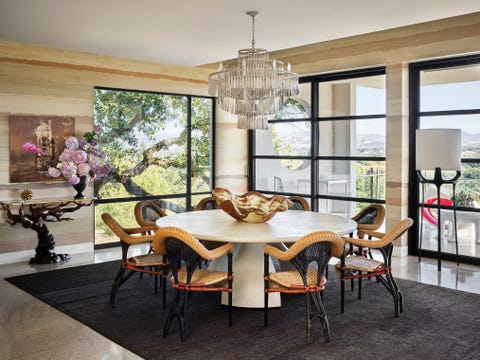 a hand painted wall mural depicts the tonal beauty of rammed earth and envelops a round dining table with chairs and a fancy chandelier hanging overhead