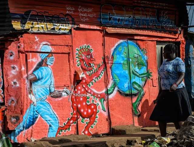 una mujer observa una pintada con el coronavirus y una corredora en kenia