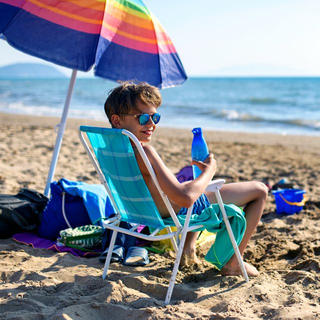 young boy sitting in beach chair under umbrella