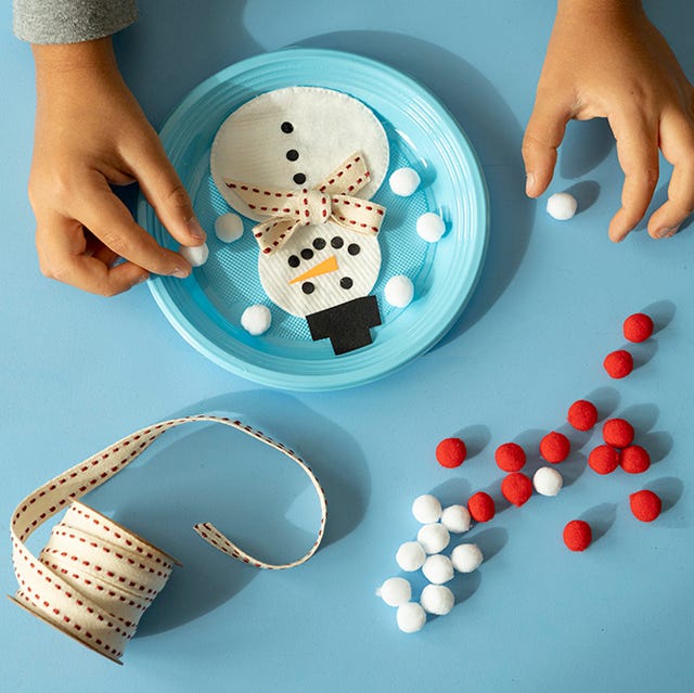 Overhead view of child hands creating a snowman toy at Christmas hands of child making a snowman with ribbon and pom pom at christmas time