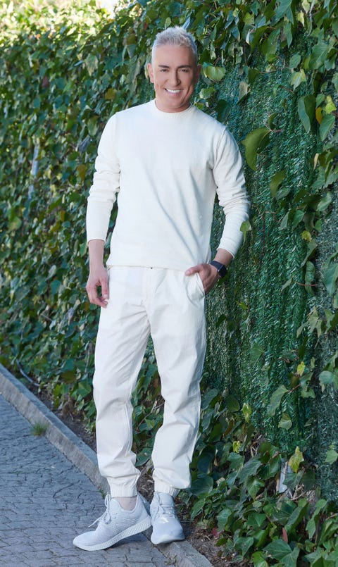 el colaborador, vestido de blanco, posa en el jardín de su casa