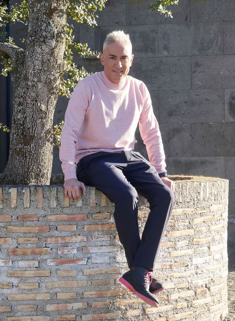 el colaborador posa sentada delante de un árbol con un jersey de color rosa