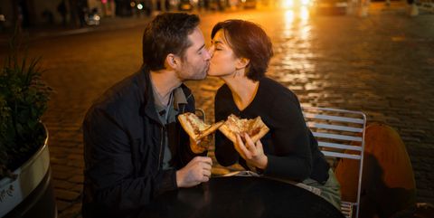 kissing couple having pizza outdoors