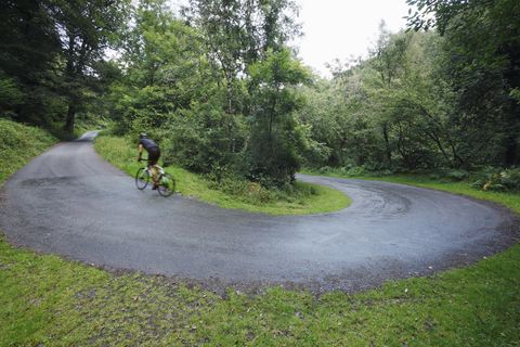 Road Cyclist cycling uphill round switchback in the road through woodland.