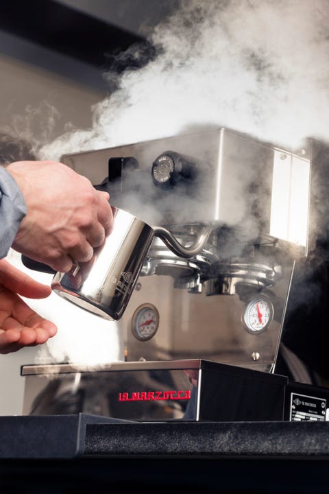espresso makinesiyle buğulanmış süt yapan kişi