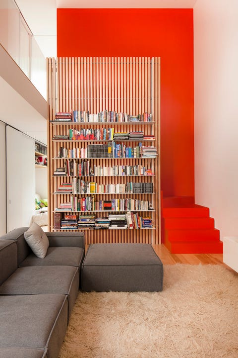 Living room with orange wall and staircase, modular sofa and slatted timber screen