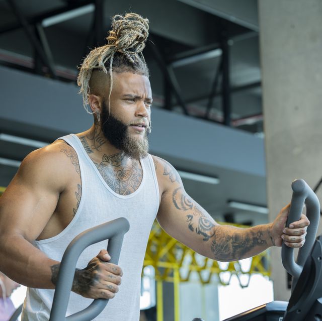 latin man with dark skin and braids trains in the gym elliptical