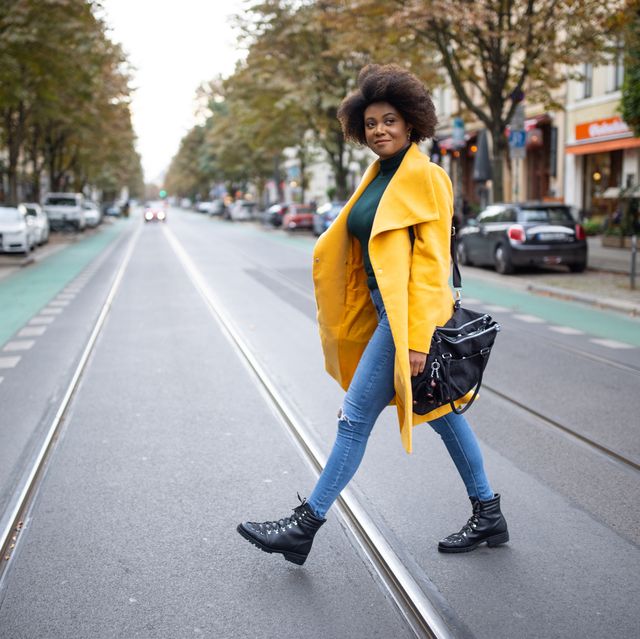woman crossing a city road in a yellow coat