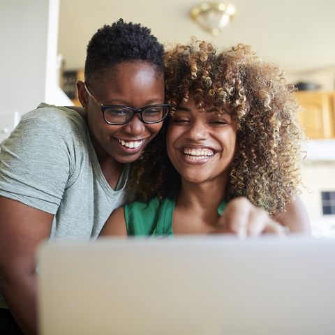 winter date ideas - Laughing Black women hugging and using laptop