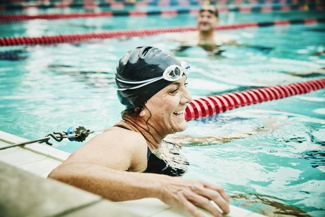 laughing mature swimmer resting between sets of early morning workout in outdoor pool