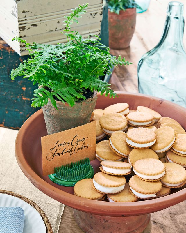 lemon creme sandwich cookies on a raised plate with a small sign and a green fern near by