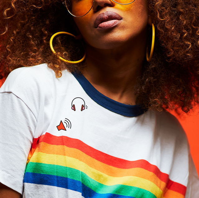 a woman in a t shirt with a rainbow on the front stands in front of a red background