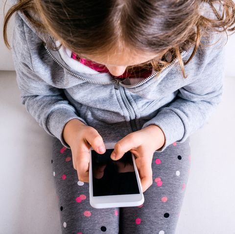 Little girl sitting on sofa, playing with smartphone