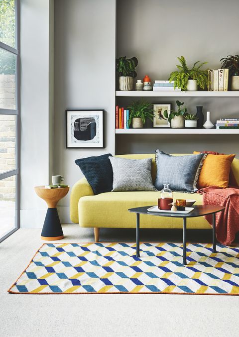 sitting room, yellow sofa white shelf behind with a blue and yellow patterned rug on the floor