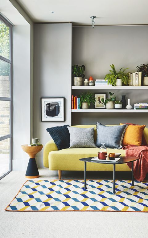 sala de estar, sofá amarelo prateleiras brancas na parte de trás com tapete estampado azul e amarelo no chão
