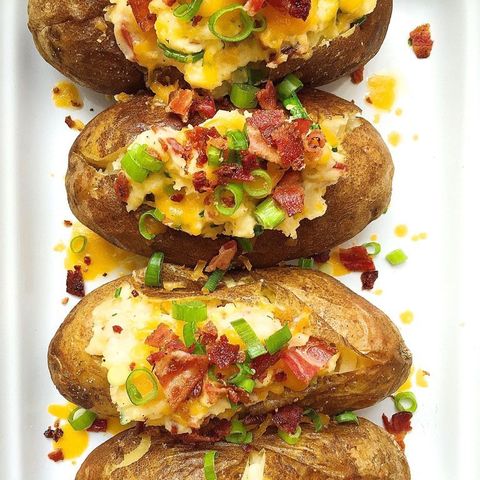 baked potatoes topped with cheese, scallions, and bacon on a white plate